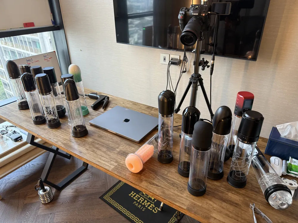 A table full of penis pumps from many brands, set up for side by side testing