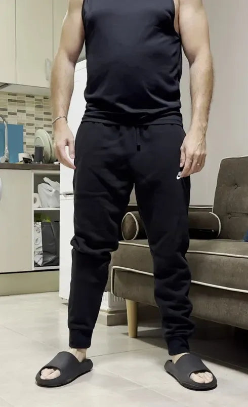 Man standing in loose black joggers wearing the Epic All Day Stretcher underneath, nothing visible